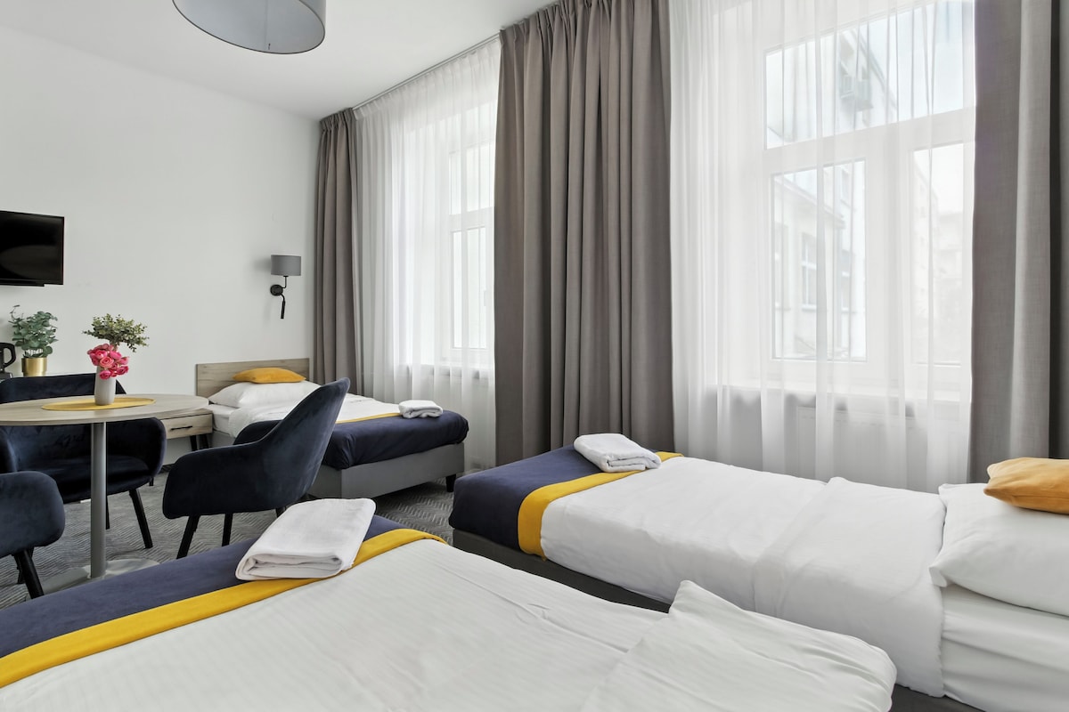 A hotel room with two beds, a desk, a chair, a TV, and a window with curtains.
