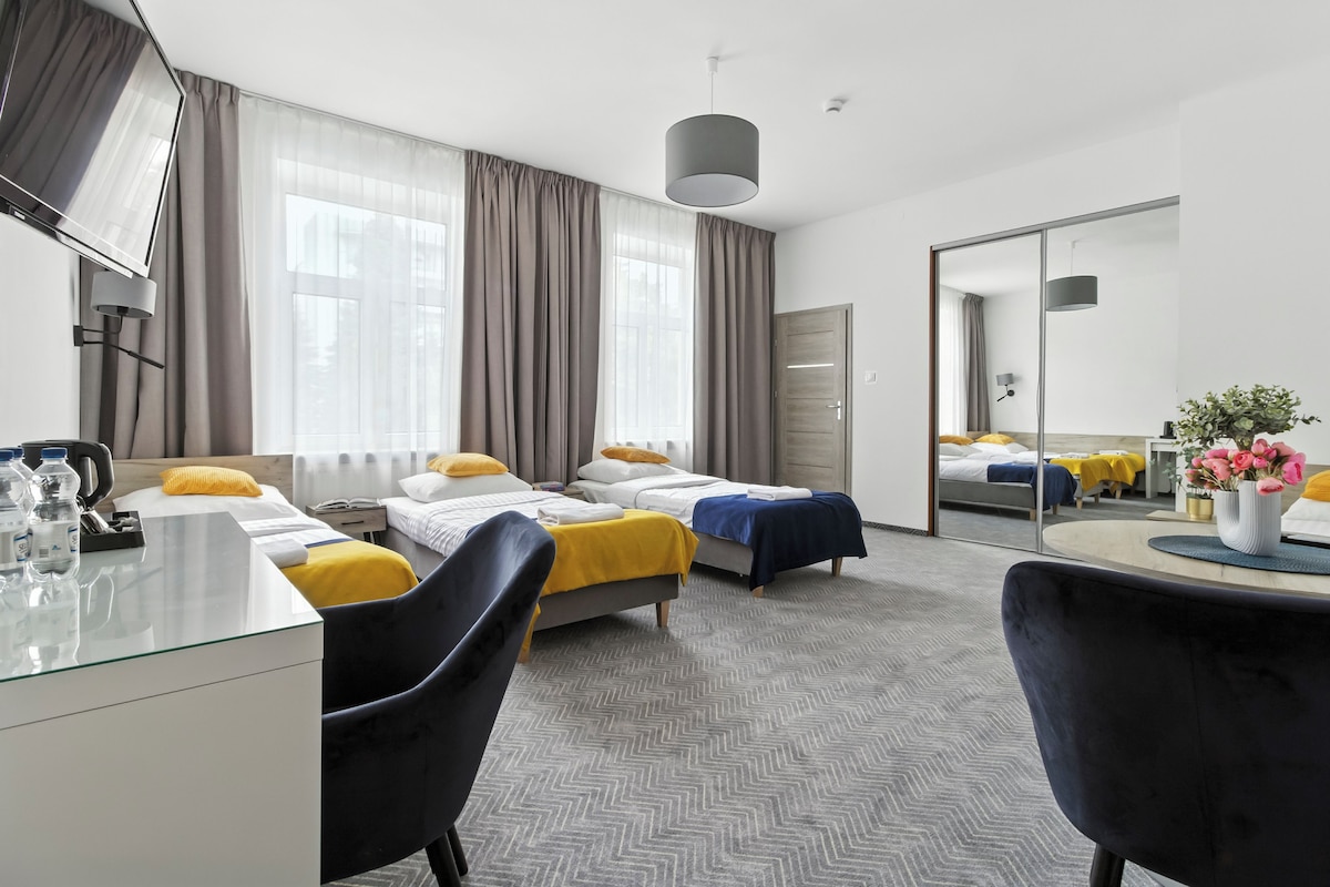 A hotel room with two beds, a desk, a chair, a mirror, and a view of the city.