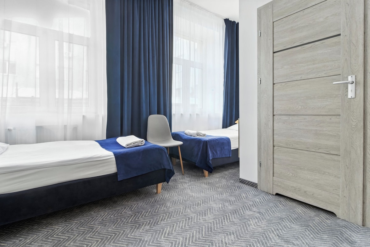 A hotel room with two beds, a chair, and a wardrobe.