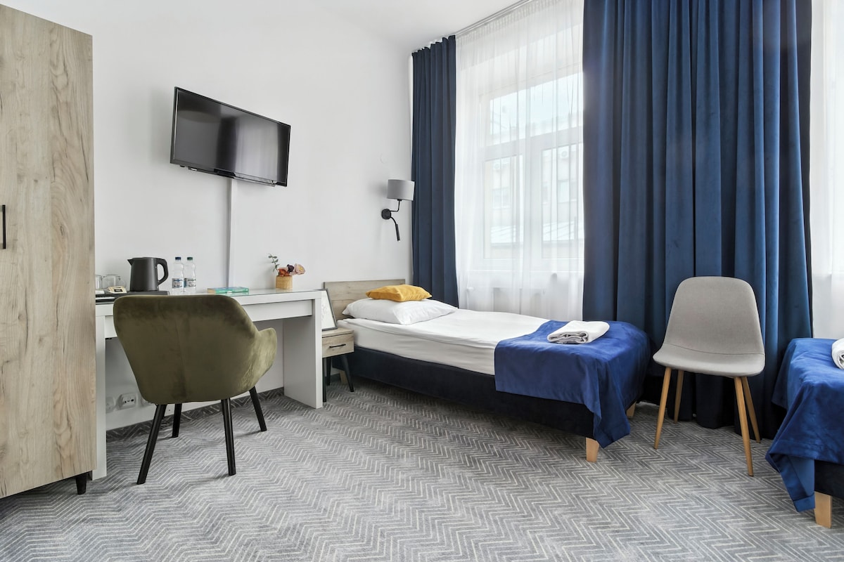 A hotel room with a bed, a desk, a chair, a TV, and a window with curtains.