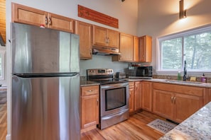 A modern kitchen with stainless steel appliances, wooden cabinets, and a granite countertop. - The Birch Haven House (Gilford)