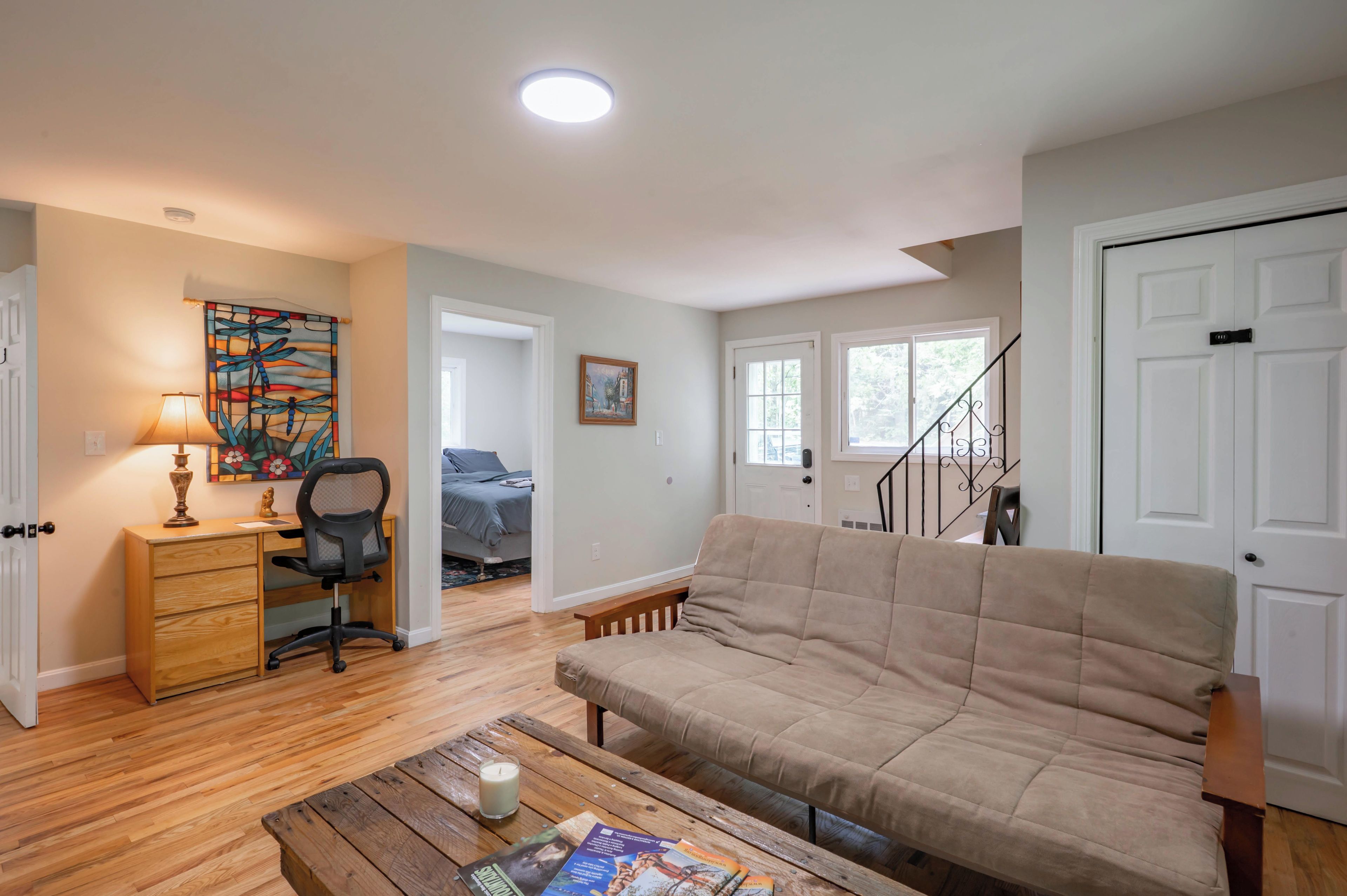 A living room with a sofa, a wooden coffee table with a candle, a desk with a lamp, and a painting on the wall.