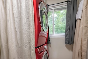Eine rote Waschmaschine in einem Badezimmer mit Fenster und Vorhängen.