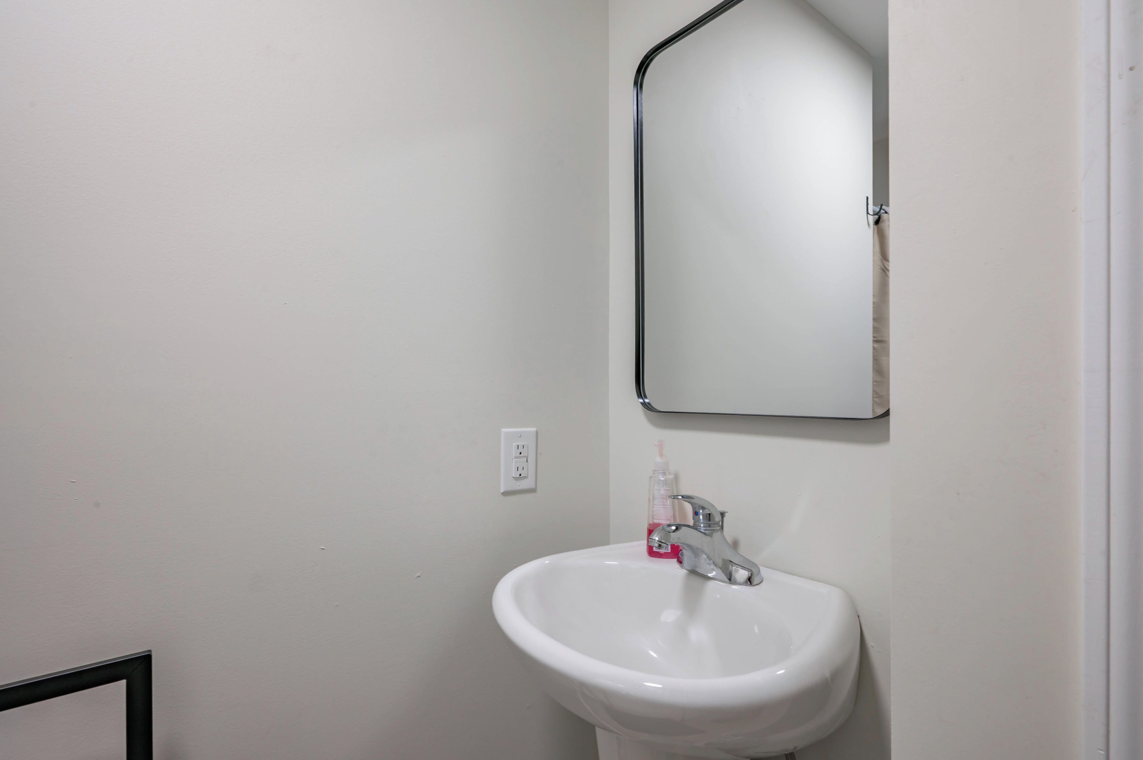 Un baño con un lavamanos blanco, un espejo y un enchufe.