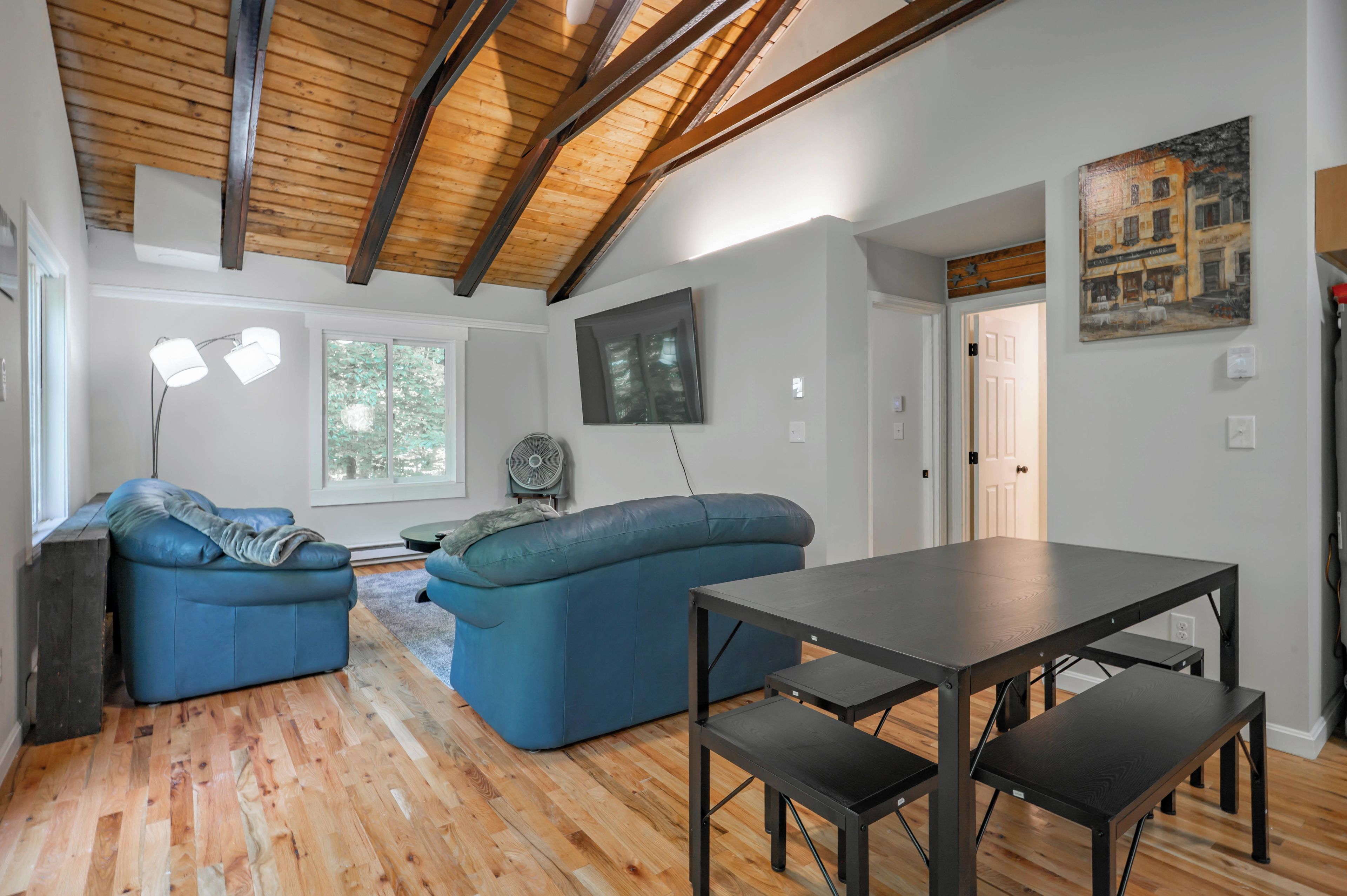 A modern living room with a wooden ceiling, a blue sofa, a dining table, and a painting on the wall.