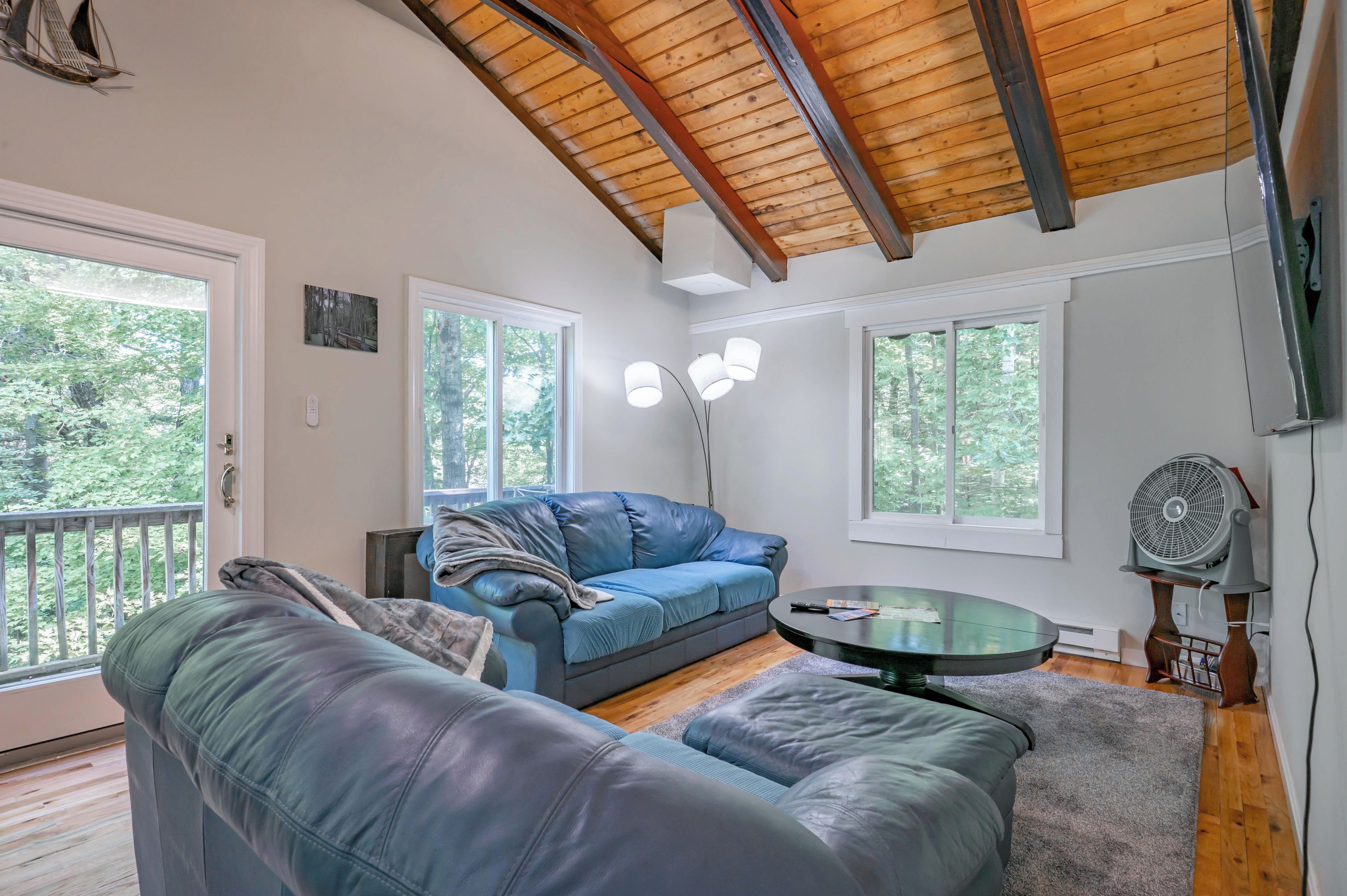 A room with a blue leather sofa, a round glass coffee table, and a wooden ceiling.