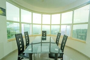 A conference room with a glass table and black chairs, large windows with a view of the city, and a white ceiling. - Devanand Villa 5BHK Mahabaleshwar (Mahabaleshwar)