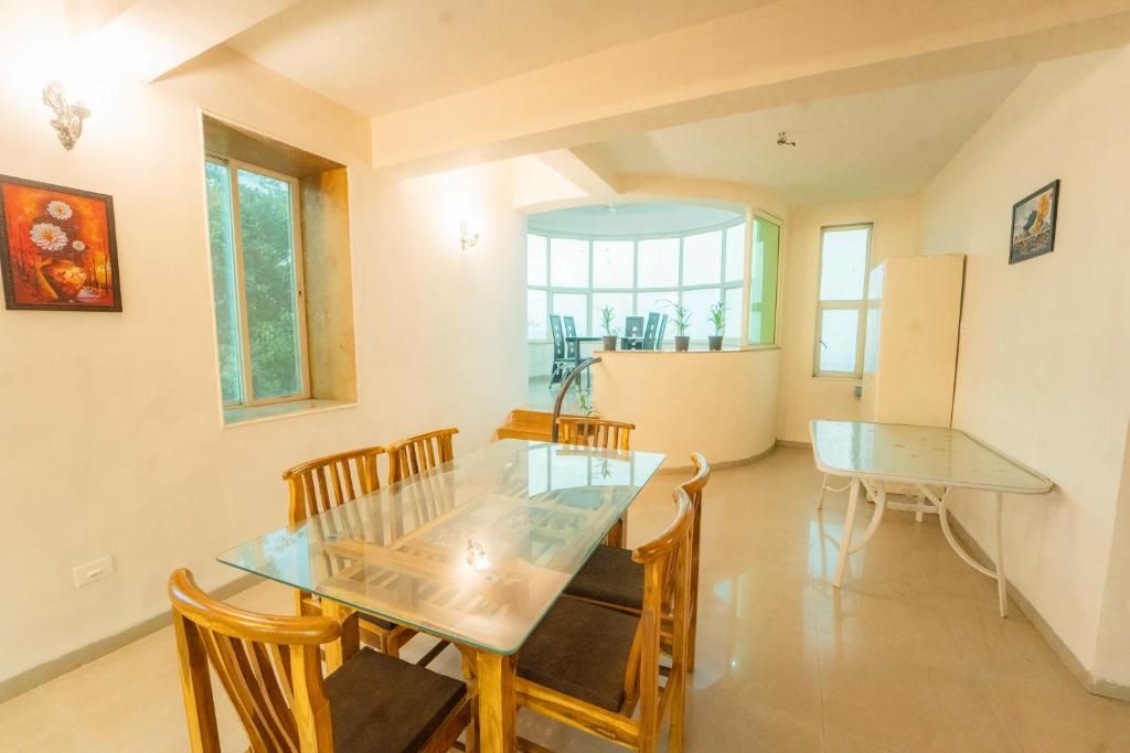 Un comedor con mesa de vidrio y sillas de madera, una mesita auxiliar y una ventana con vistas a zonas verdes.