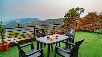 A terrace with a table and chairs, potted plants, and a view of the hills.