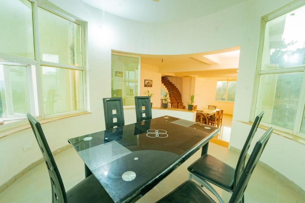Un comedor con una mesa y sillas de vidrio, una escalera al fondo y vista al exterior.