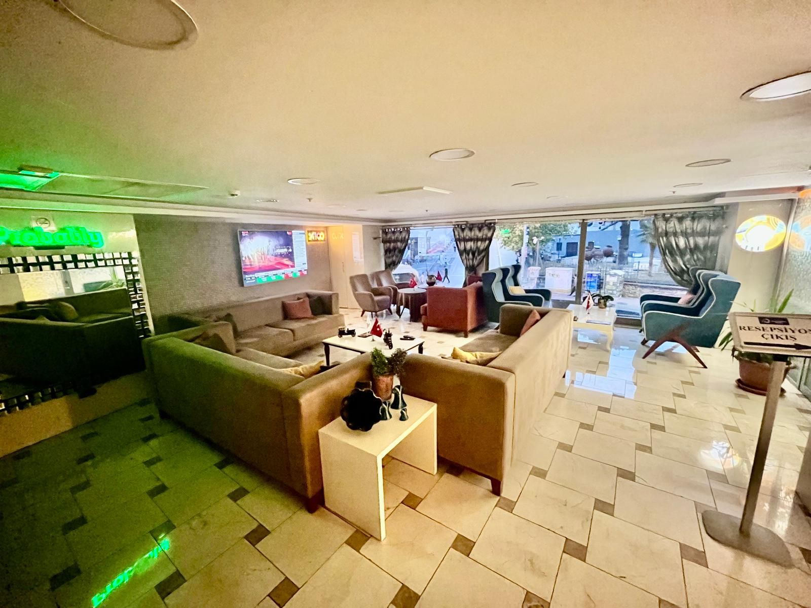A hotel lobby with a seating area, a television screen, and a view of the outside.