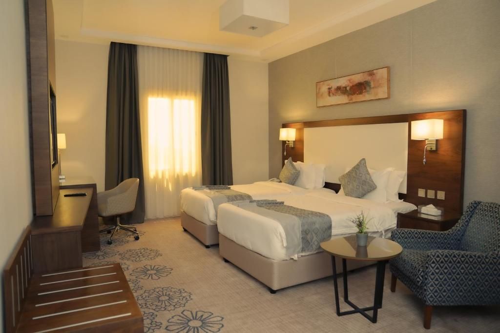 A hotel room with a bed, two bedside tables, a chair, a desk, and a small table with a plant.