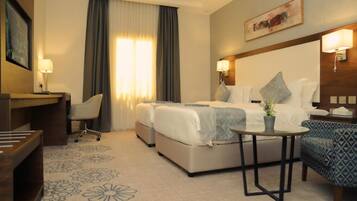A hotel room with a bed, a desk, a chair, a small table, and a large window with curtains.
