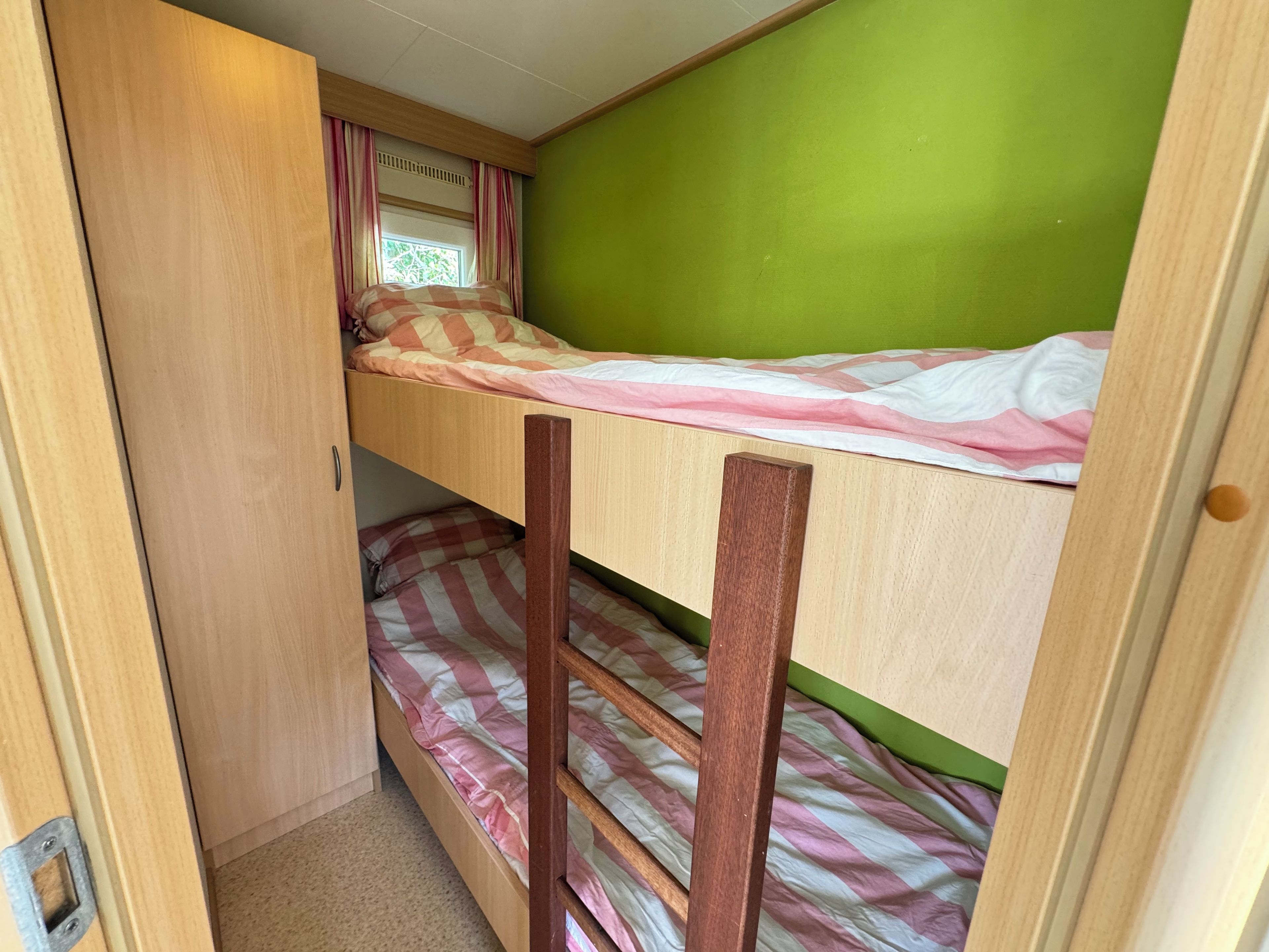 A bunk bed with a window and curtains, a green wall, and a wooden door.