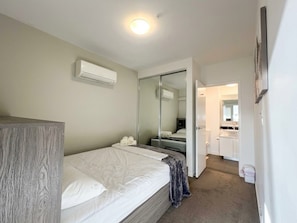 A bedroom with a bed, a wardrobe, an air conditioning unit, a mirror, and a bathroom visible through a glass door. - Luxury High Rise Suite & CBD Open Views. (Melbourne)