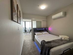 A hotel room with a bed, a desk, and a chair. There is a window and an air conditioning unit on the wall. - Luxury High Rise Suite & CBD Open Views. (Melbourne)