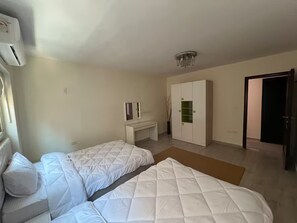 Un dormitorio con dos camas, un escritorio, un armario y una puerta que da a otra habitación.