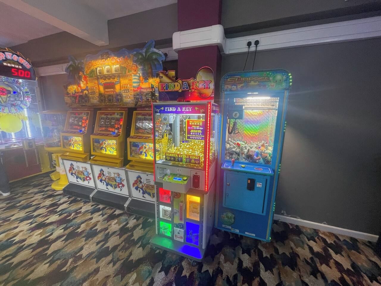 A row of brightly lit arcade machines in a room with patterned carpet flooring.