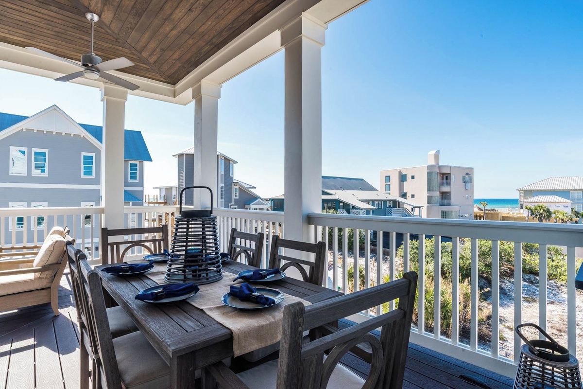 A covered outdoor dining area with a table set for four, overlooking a beach.
