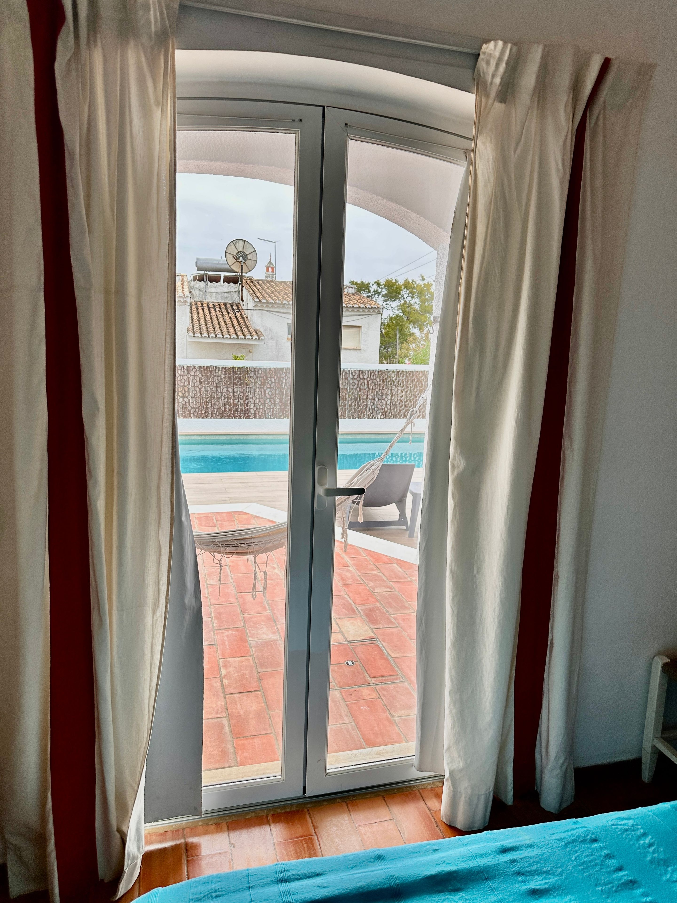 A room with a sliding glass door leading to an outdoor area with a pool, a hammock, and a chair.
