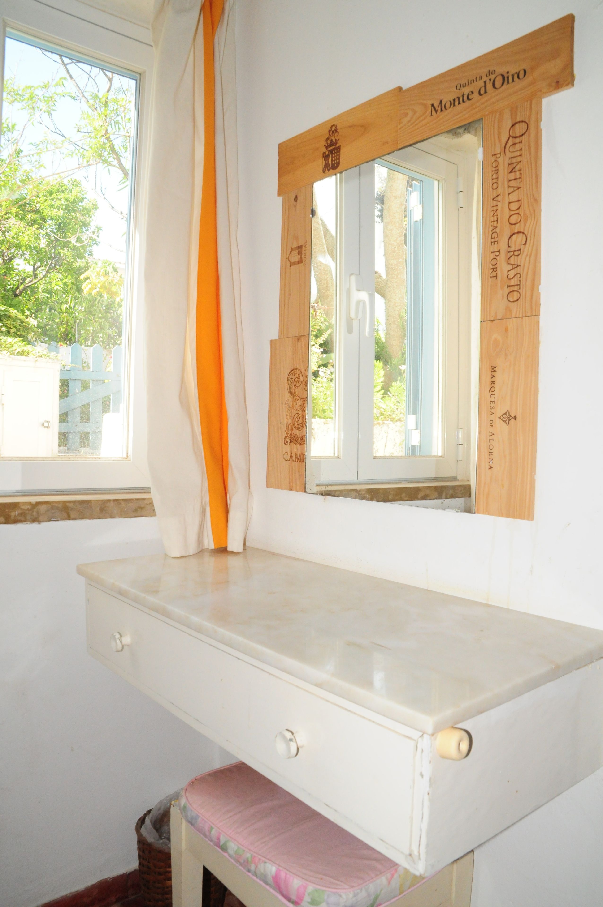 Una habitación con ventana, un escritorio blanco con cajones y una silla rosa.