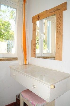 Una habitación con ventana, un escritorio blanco con cajones y una silla rosa.