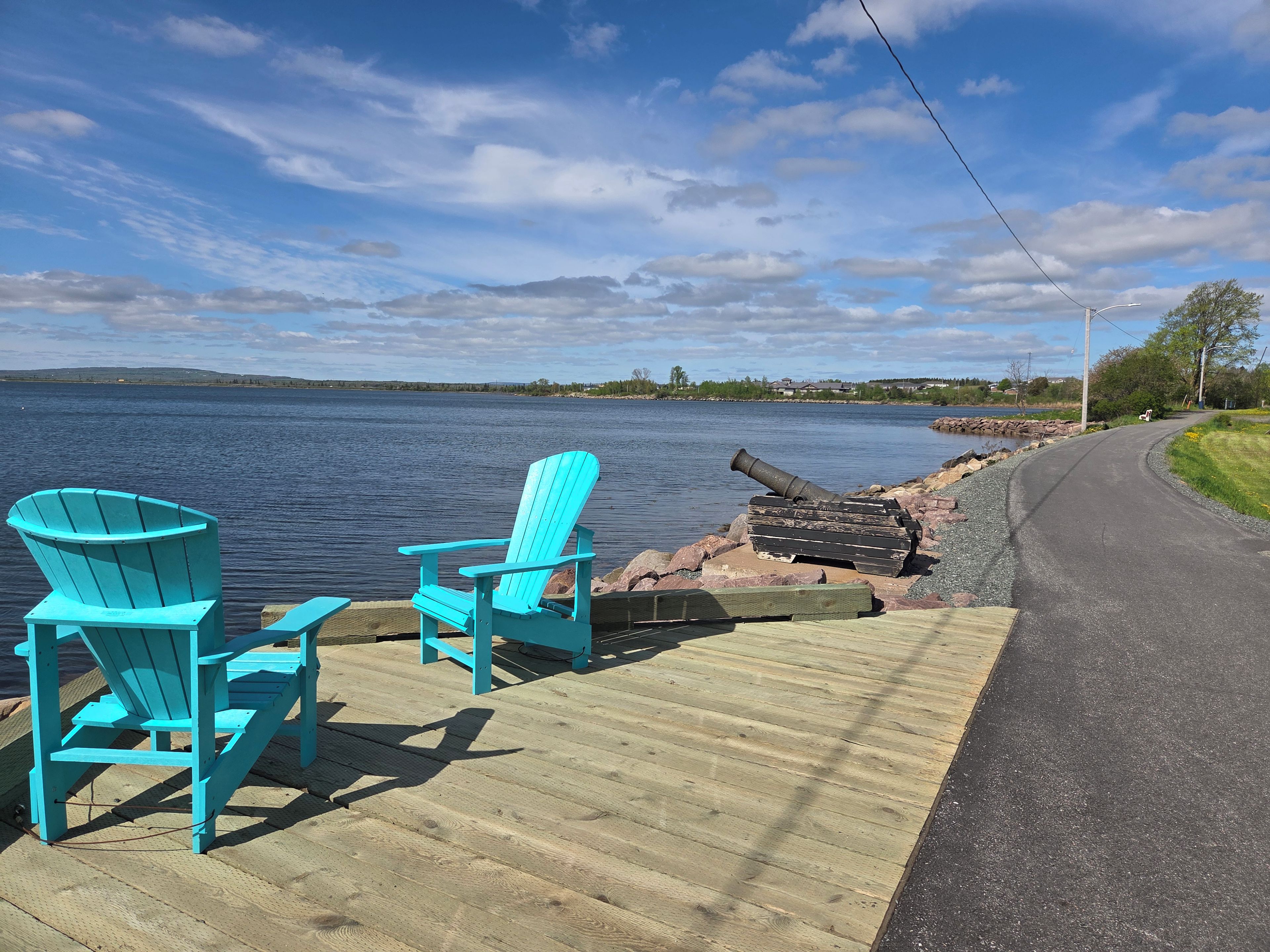 Un muelle de madera con dos sillas Adirondack turquesas dando a un lago tranquilo.