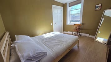 Une chambre à coucher avec un lit en bois, une chaise, une fenêtre avec des stores et une porte.