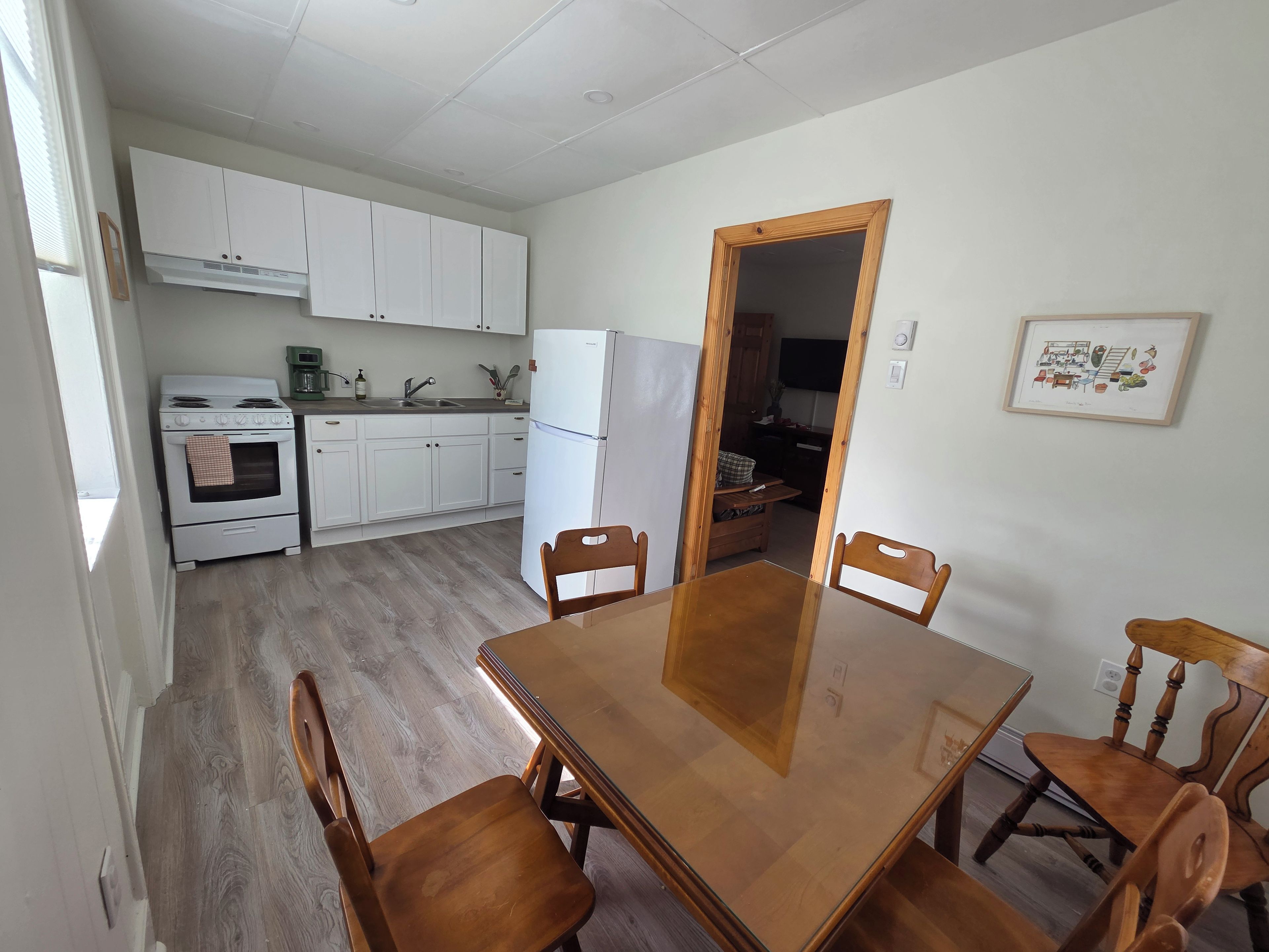 Une cuisine avec des meubles blancs, une cuisinière, un réfrigérateur et une table à manger avec des chaises.