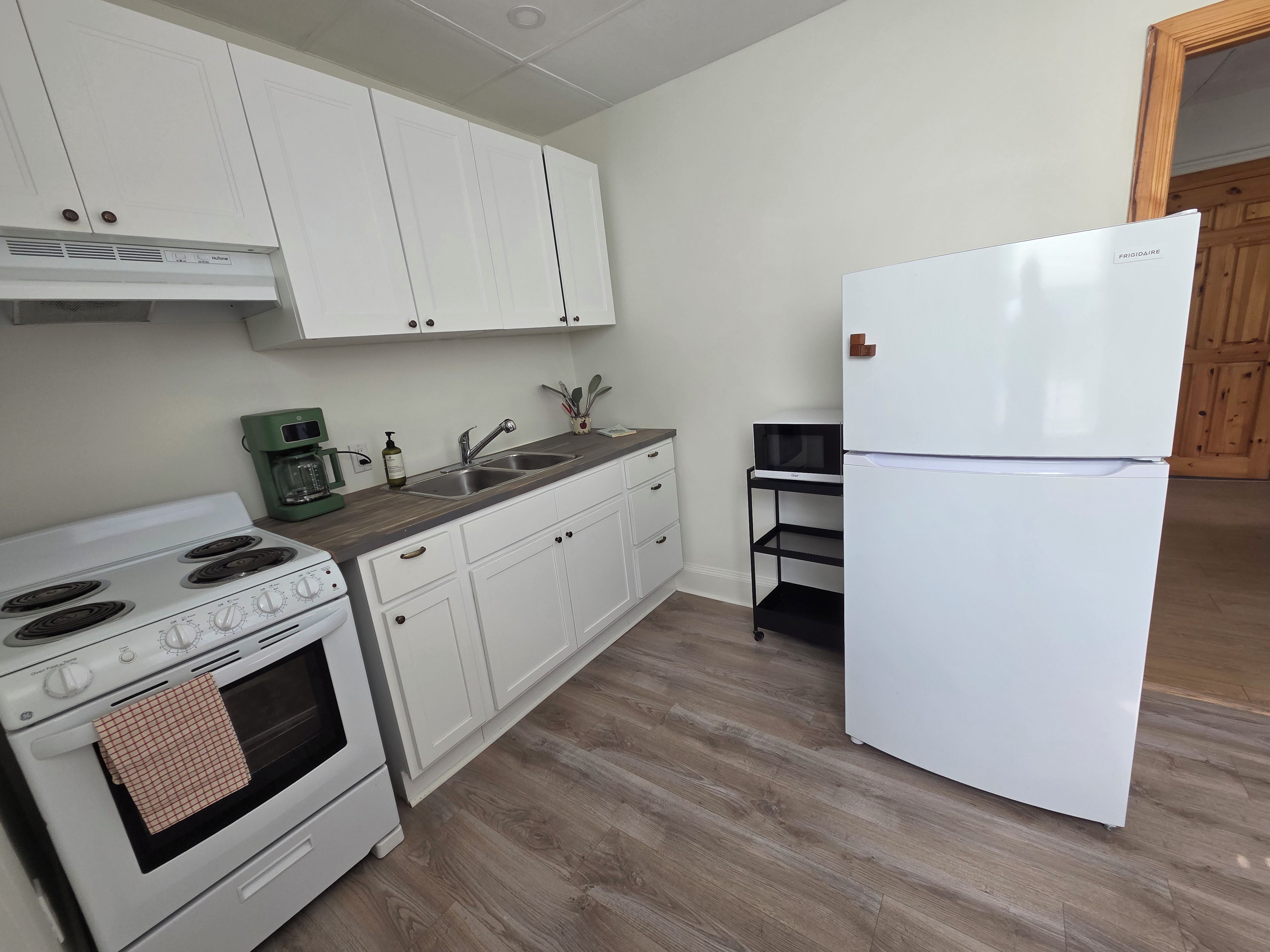 A kitchen with white cabinets, a white refrigerator, a stove, a sink, and a microwave on a black shelf.