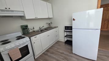 A kitchen with white cabinets, a white refrigerator, a stove, a sink, and a microwave on a black shelf.