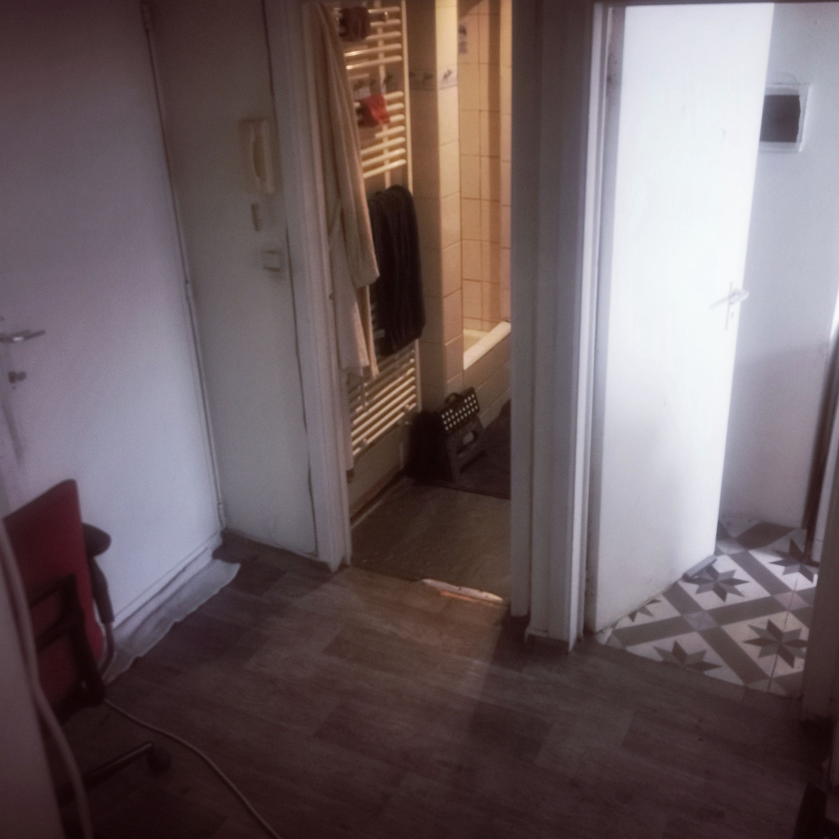 A narrow hallway with a tiled floor, a door leading to a bathroom, and a red chair.