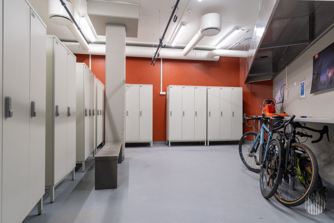 A clean, modern restroom with multiple lockers, a bench, and bicycles parked against the wall.