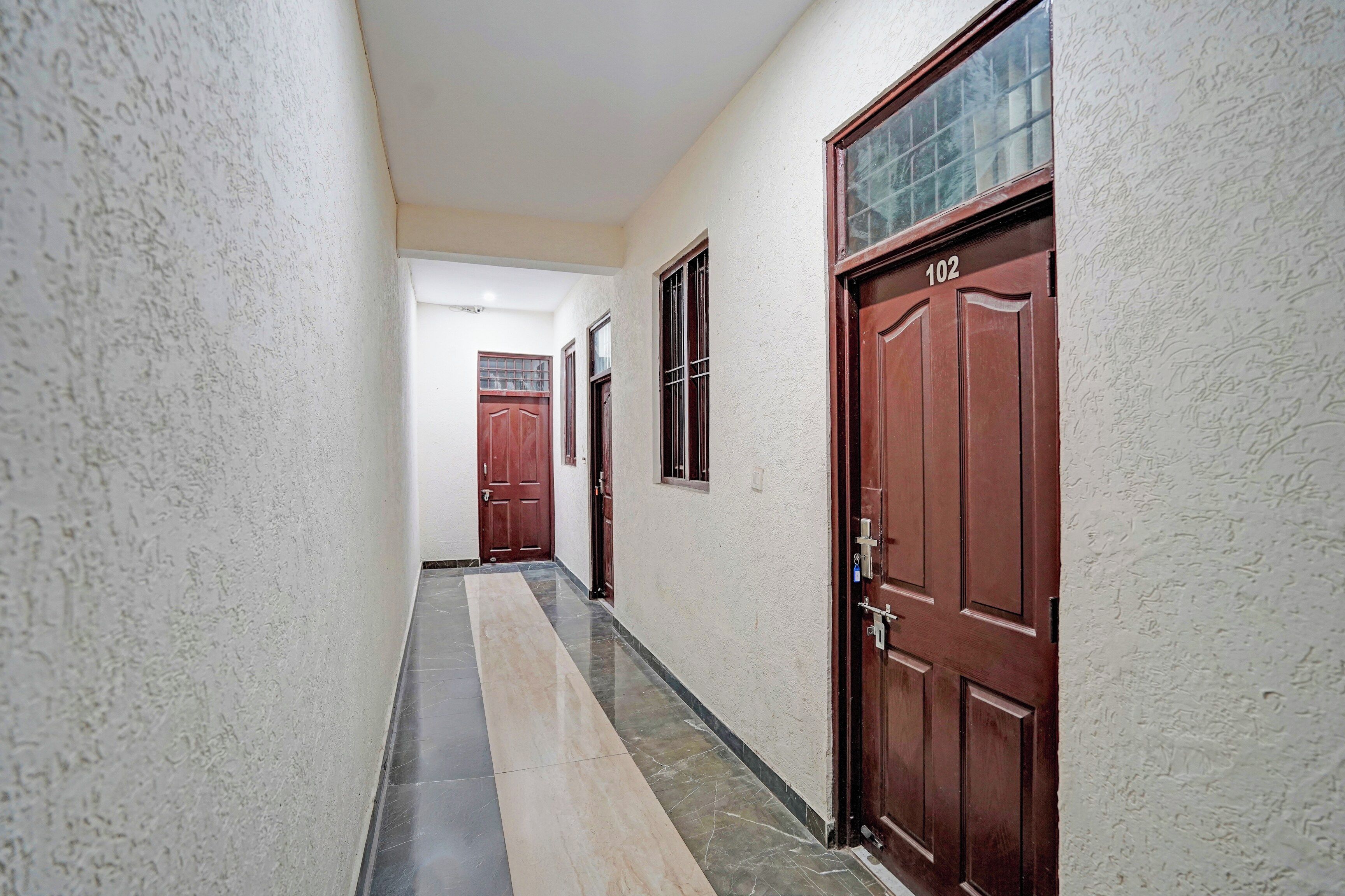 A corridor with a tiled floor, two wooden doors, and a window with bars.