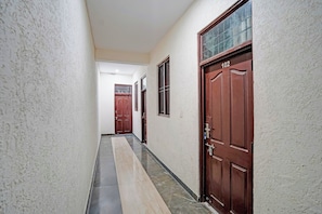 A corridor with a tiled floor, two wooden doors, and a window with bars. - Hotel O Starline (Zirakpur)
