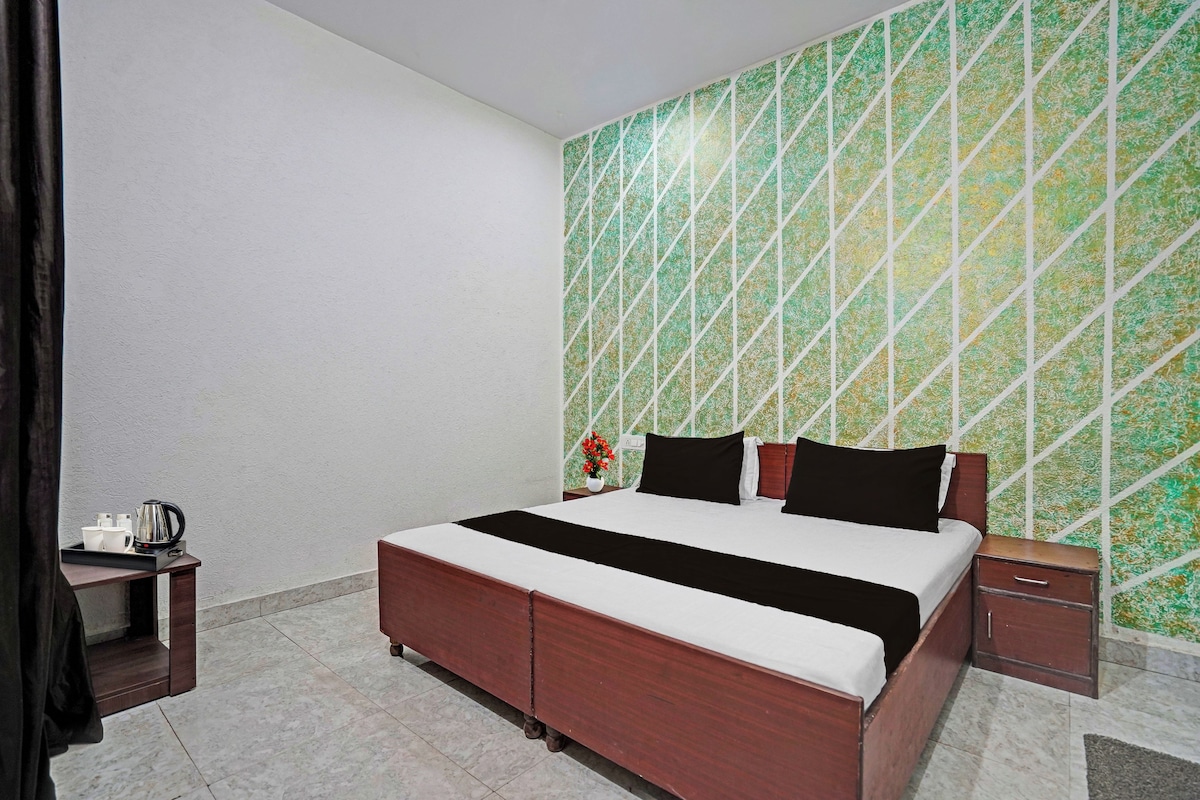 A hotel room with a bed, bedside tables, a small table with a kettle and cups, and a patterned wall.