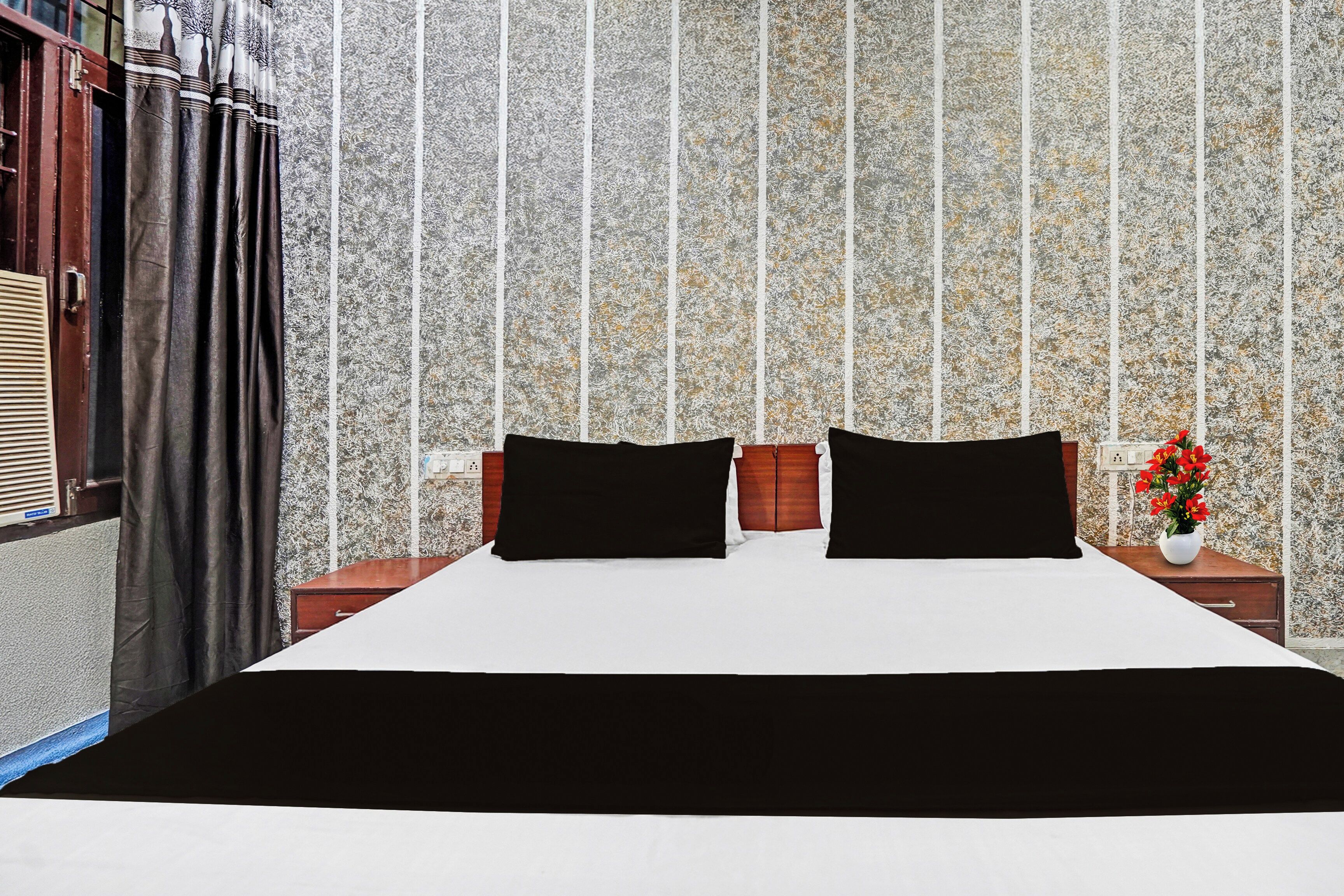 A hotel room with a large bed, two bedside tables, a nightstand, a window with curtains, and a wall with a textured pattern.