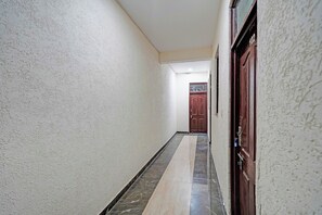 Un pasillo con piso de mármol, una puerta de madera y una pared blanca con textura.