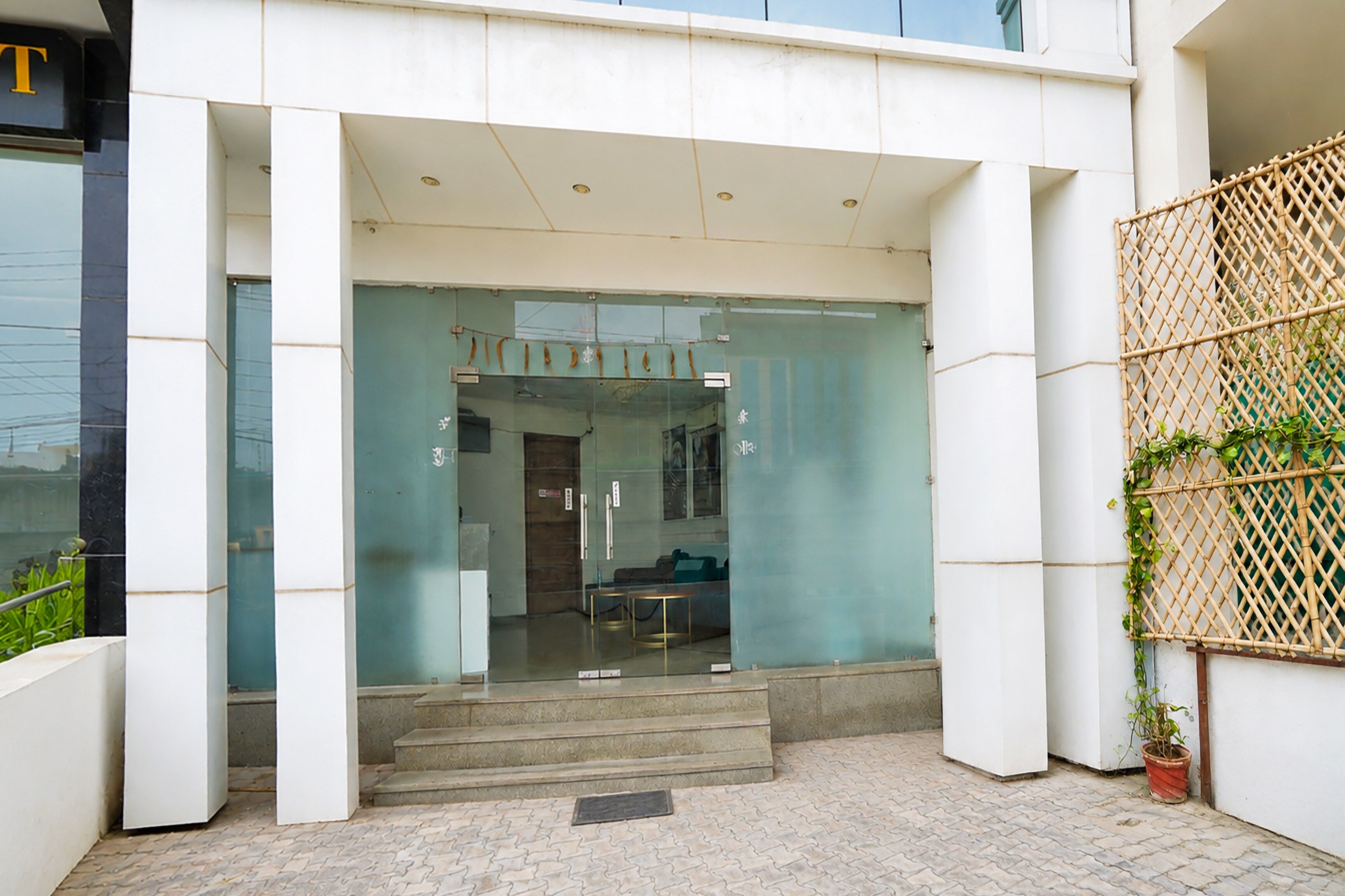 Entrada de un edificio con puerta de vidrio, varios escalones que conducen a ella y una valla de bambú a la derecha.