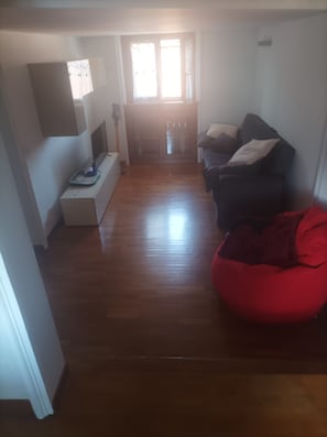 Uma sala de estar com um sofá, um puff vermelho e uma TV em um suporte.