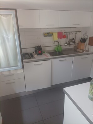 Uma cozinha com armários brancos, bancada preta e diversos utensílios pendurados acima da pia.
