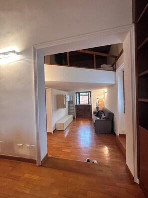 Uma sala de estar ampla, com teto alto, piso de madeira e um banco embutido.