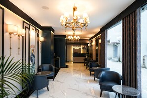 Vestíbulo de hotel con candelabro, zona de estar, mostrador de recepción y vista a la calle.