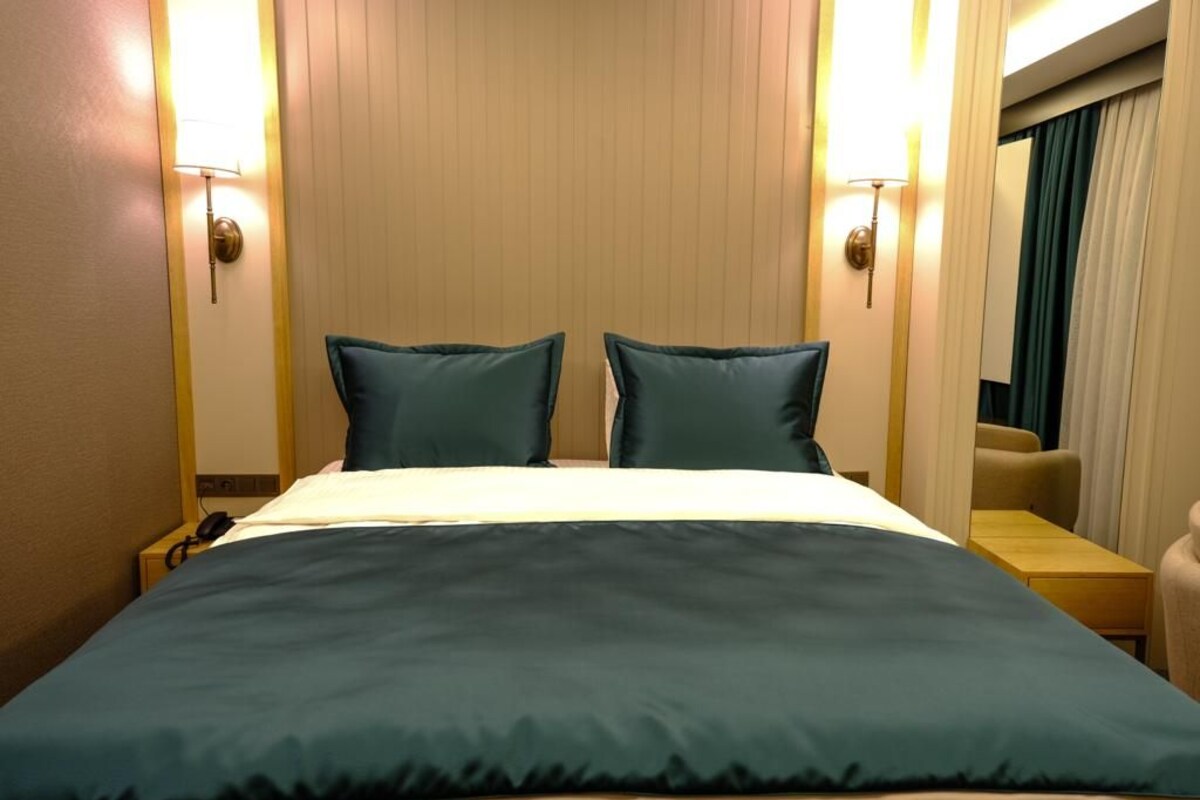 Una habitación de hotel con una cama, dos almohadas, una mesita de noche, una lámpara y una silla.