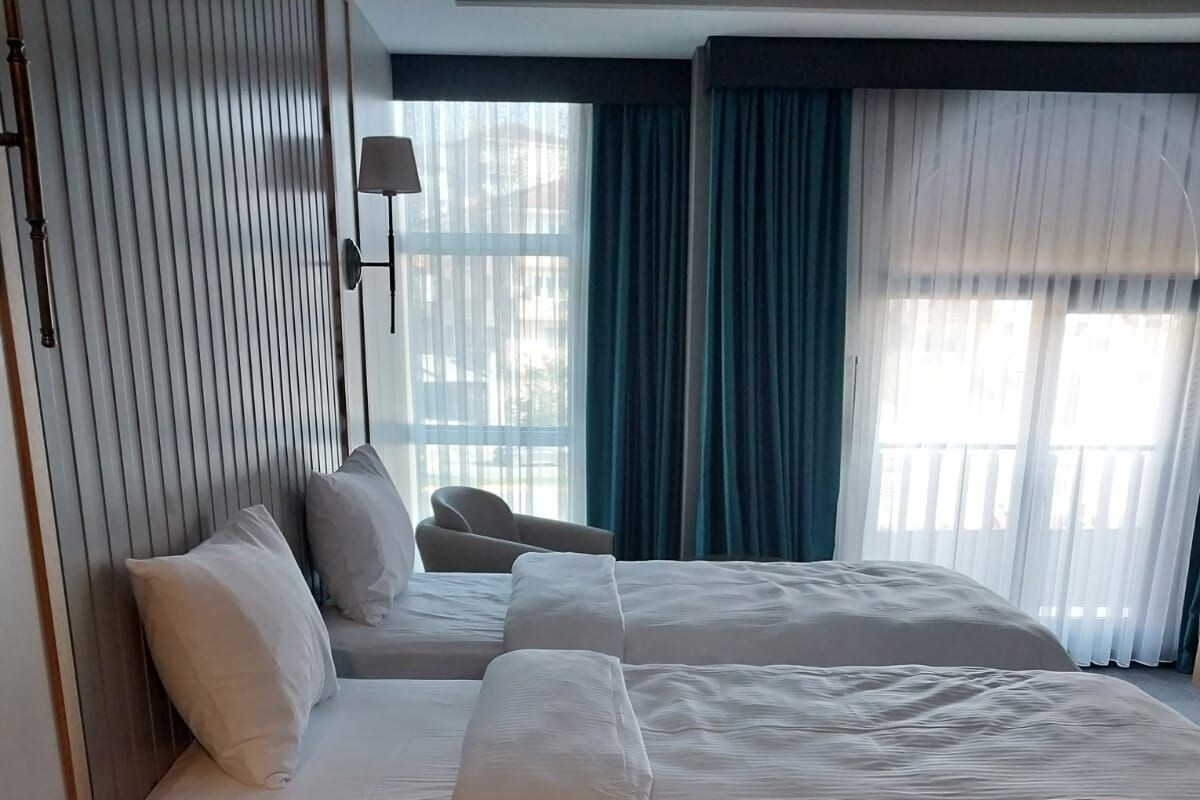 Habitación de hotel con dos camas, una mesita de noche con teléfono y vistas al exterior a través de amplias ventanas.