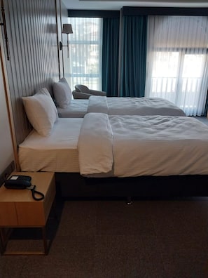 Habitación de hotel con dos camas, una mesita de noche con teléfono y vistas al exterior a través de amplias ventanas.