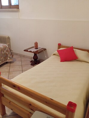 Un dormitorio con cama de madera, una mesita de noche con lámpara y una silla con funda estampada.