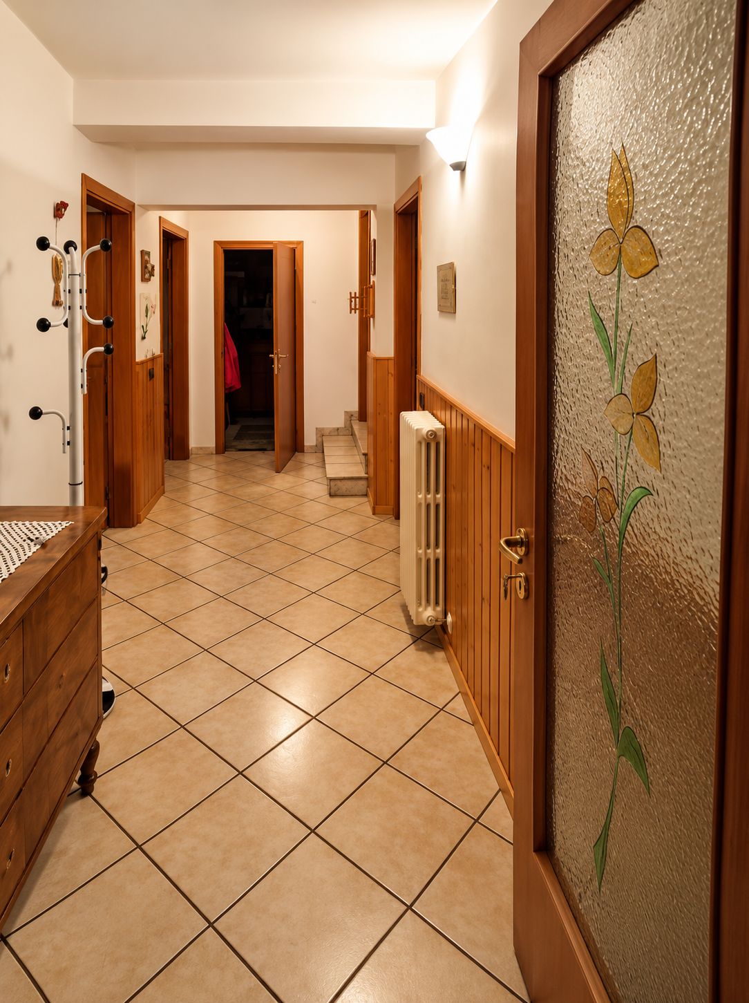 Un couloir avec un radiateur, des portes en bois et un sol carrelé.