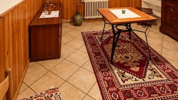 Et værelse med træpaneler, en radiator, et bord med måtte, et skab og et vindue med persienner.