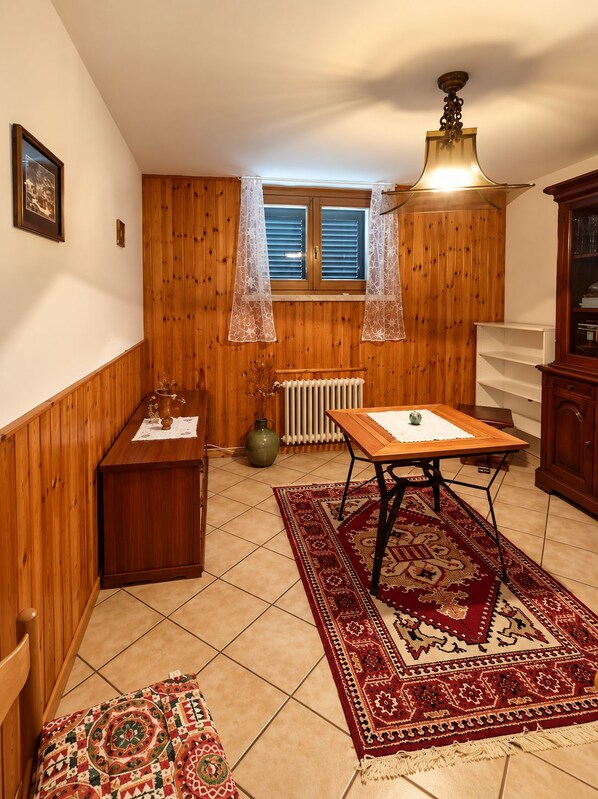 Una habitación con paredes de madera, un radiador, una mesa con alfombra, un armario y una ventana con persianas.